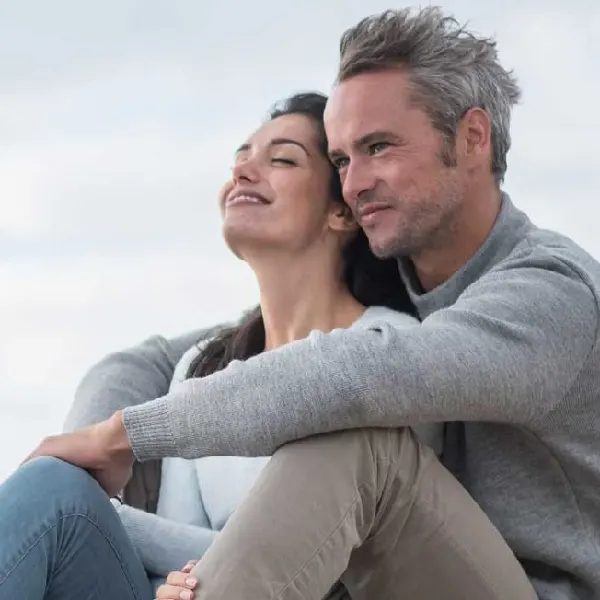 Pareja abrazada con ropa de invierno a merced del viento en una colina