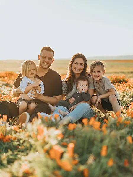Joven familia de cinco miembros sentados en un campo de flores naranjas en actitud feliz
