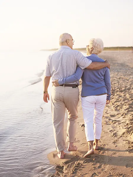 Pareja de ancianos paseando por la playa junto al mar con los pies descalzos