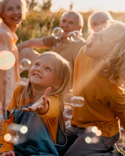 Niños jugando con pompas de jabon en un campo observados por su madre junto a sus abuelos