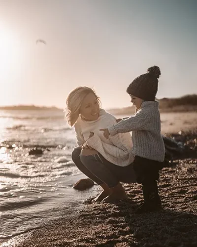 Mujer con su hijo a la orilla de la playa al atardecer con ropa de abrigo