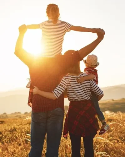 Familia de espaldas abrazados y con sus dos hijos en brazos sobre un campo al atardecer