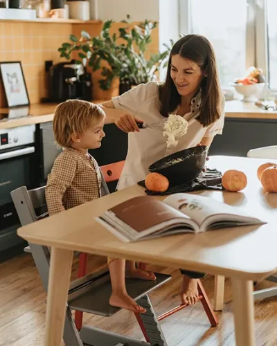 Mujer feliz preparando una receta en la mesa de la cocina observada por su hijo pequeño