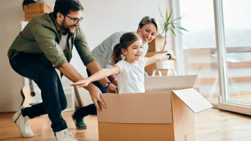 Pareja feliz jugando con su hija metida en una caja de carton en el salon de su hogar