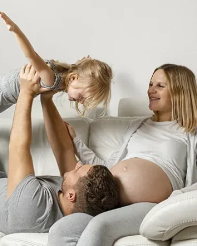 Familia de tres miembros embarazada en el sofa jugando con una niña pequeña