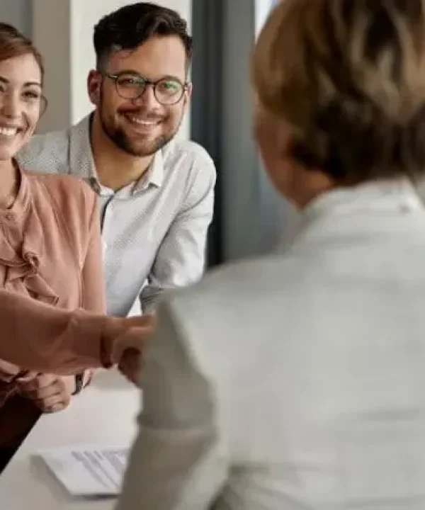 Joven pareja cerrando un acuerdo con una mujer de espaldas en un despacho