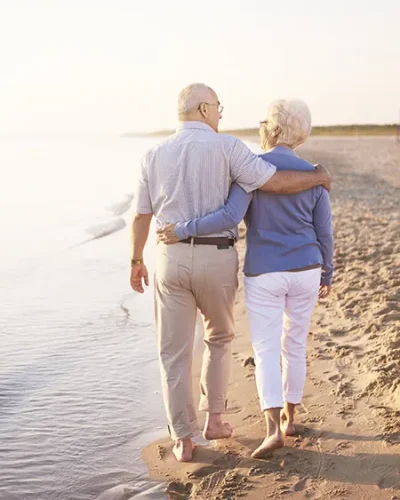 Pareja de ancianos paseando por la playa junto al mar con los pies descalzos