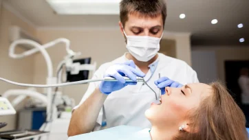 Dentista en su consulta trabajando sobre una paciente con intrumental en su boca