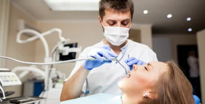 Dentista en su consulta trabajando sobre una paciente con intrumental en su boca